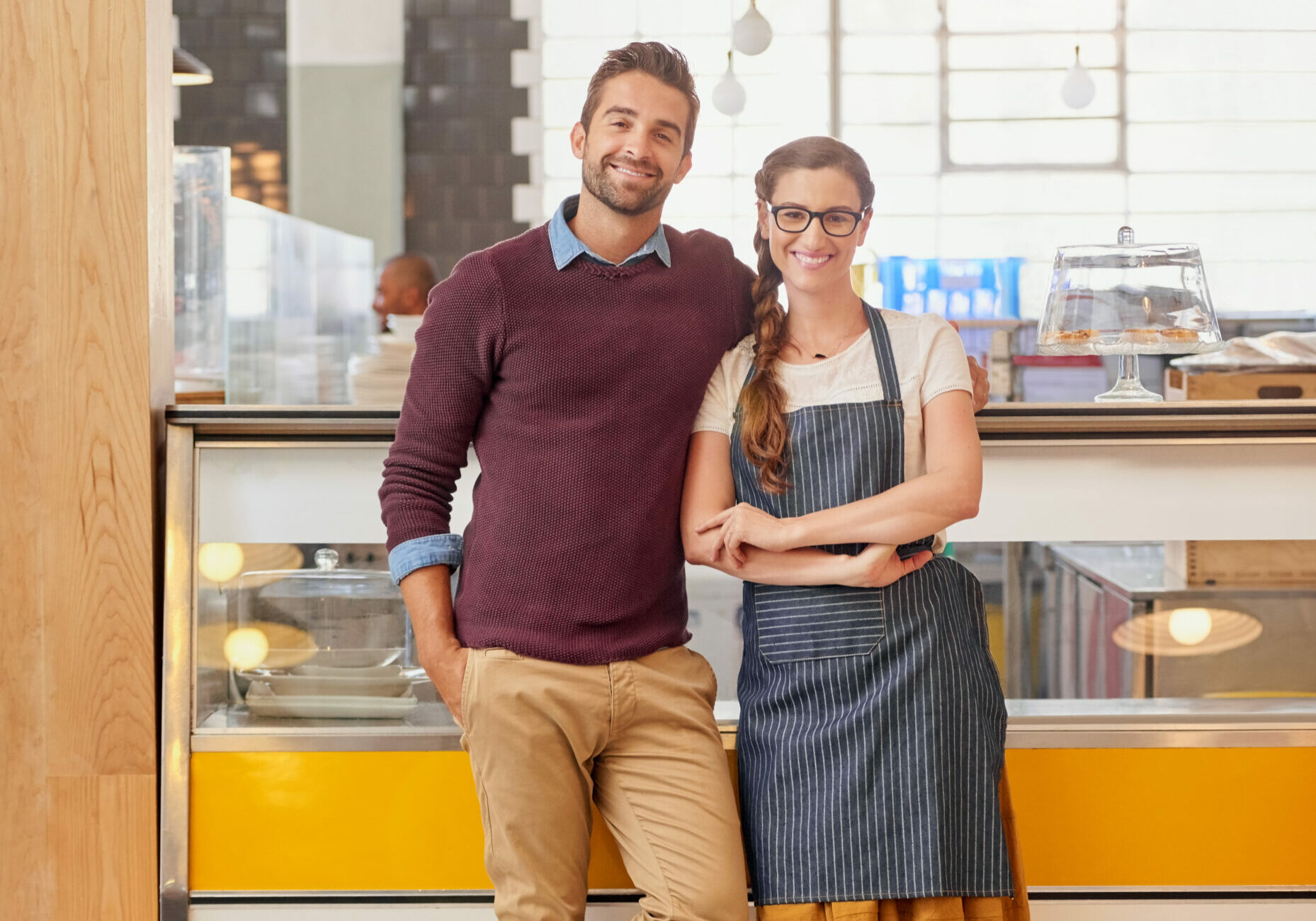 Portrait of two young business owners posing in front of the counter in their coffee shop.