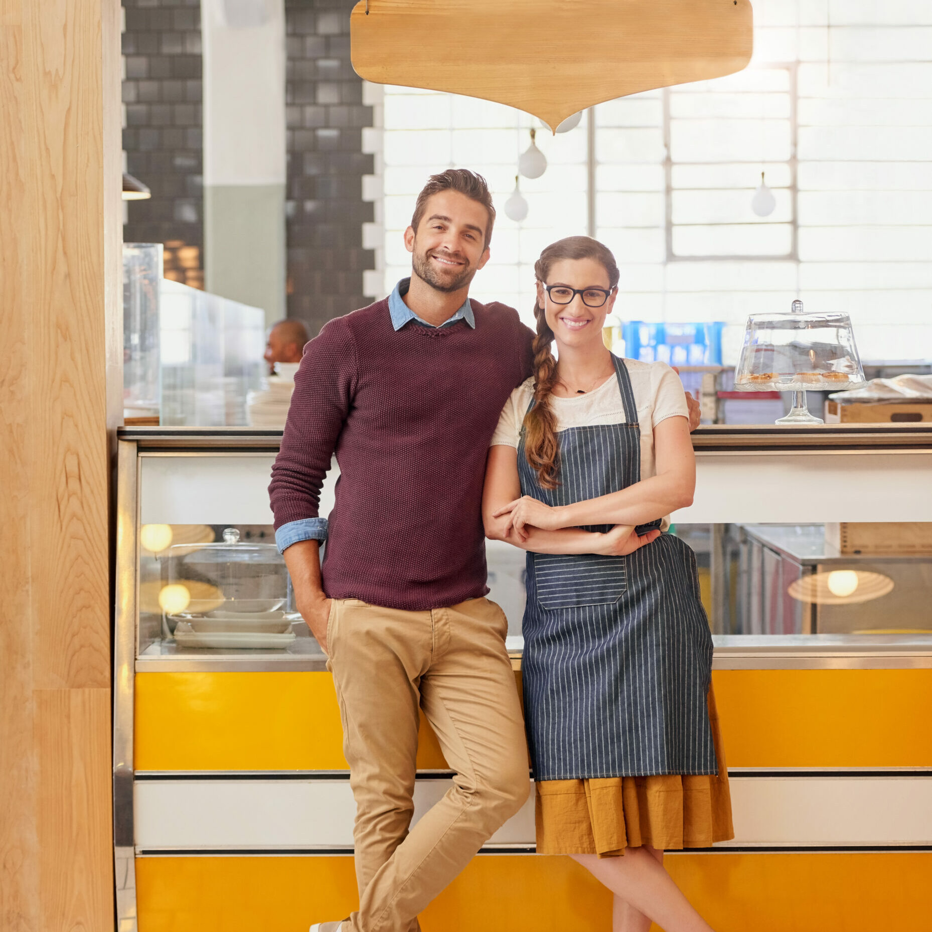 Portrait of two young business owners posing in front of the counter in their coffee shop.